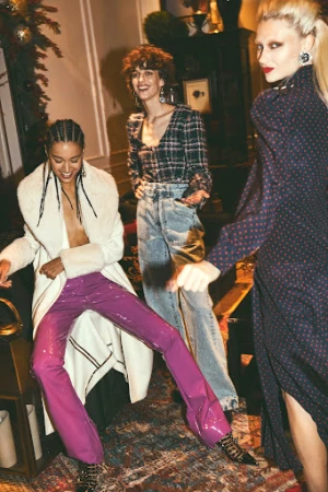 Three women laughing and dancing in a warmly lit living room, photographed by Stefano Galuzzi.
