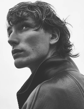 Close-up black and white portrait of a man wearing a textured leather jacket with a high collar, looking upward.