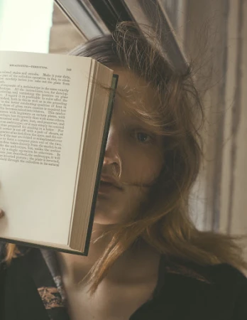 Close-up portrait of a woman holding an open book across her face, by Stefano Galuzzi