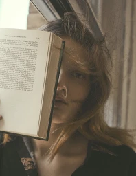 Close-up portrait of a woman holding an open book across her face, by Stefano Galuzzi
