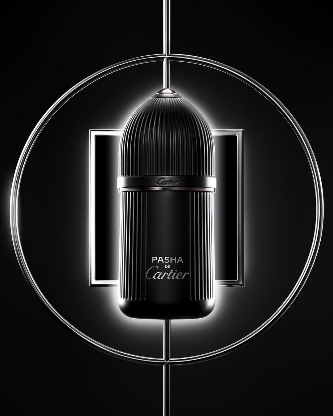 Elegant close-up of a black Pasha de Cartier fragrance bottle with fluted texture, highlighted by a circular metal frame against a dark backdrop.