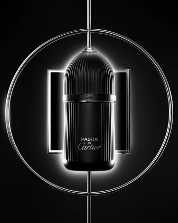 Elegant close-up of a black Pasha de Cartier fragrance bottle with fluted texture, highlighted by a circular metal frame against a dark backdrop.