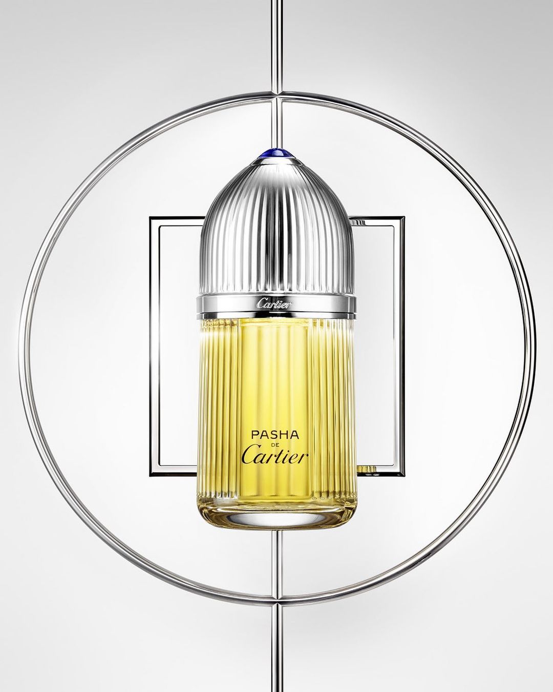 Elegant studio shot: Cartier Pasha perfume bottle with silver ridged cap, suspended in a silver ring, against a gradient gray background.