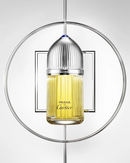 Elegant studio shot: Cartier Pasha perfume bottle with silver ridged cap, suspended in a silver ring, against a gradient gray background.