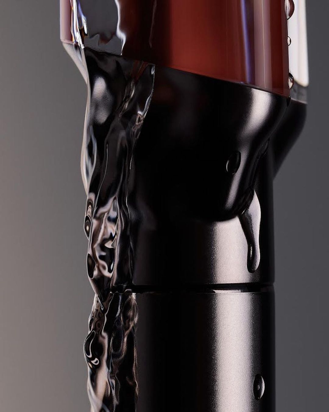 Close-up product shot of a brown and black bottle with transparent liquid running down the side, against a gray background.