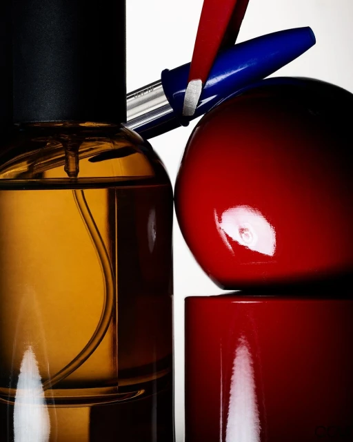 Product shot featuring a glass amber bottle, a red sphere and rectangle, and a blue and silver pen against a clean white backdrop.