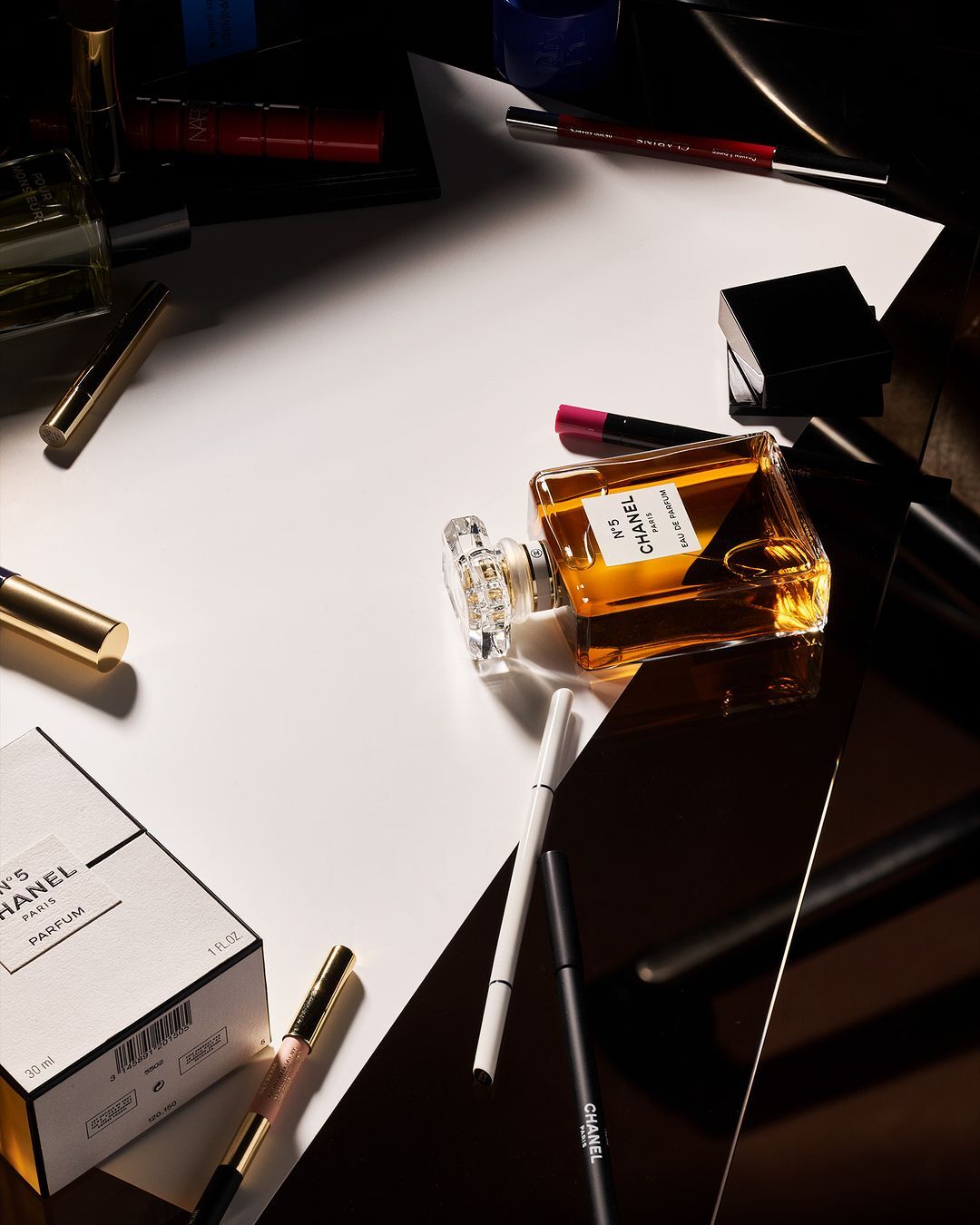 Still life shot of Chanel No. 5 perfume bottle with cosmetics on a split white and black background, product photography, beauty industry.