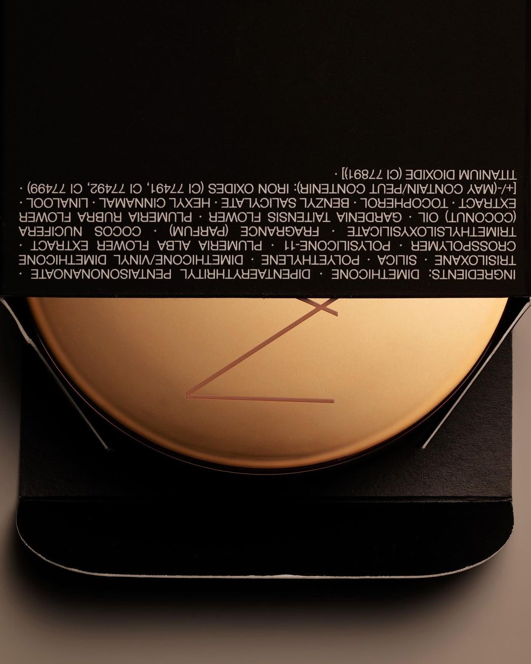 Close-up of NARS beauty product compact, featuring a bronzed metallic finish and minimalist design against a dark background.