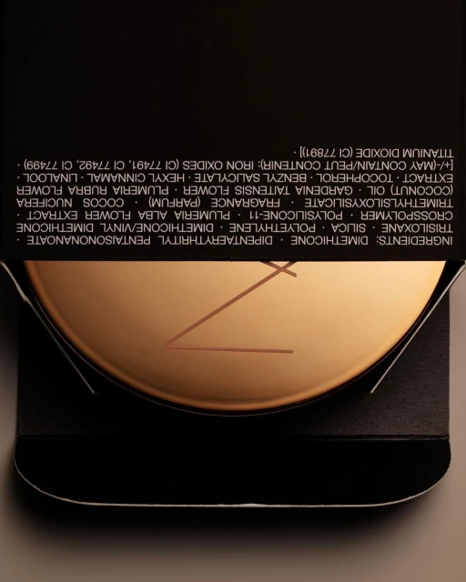 Close-up of NARS beauty product compact, featuring a bronzed metallic finish and minimalist design against a dark background.
