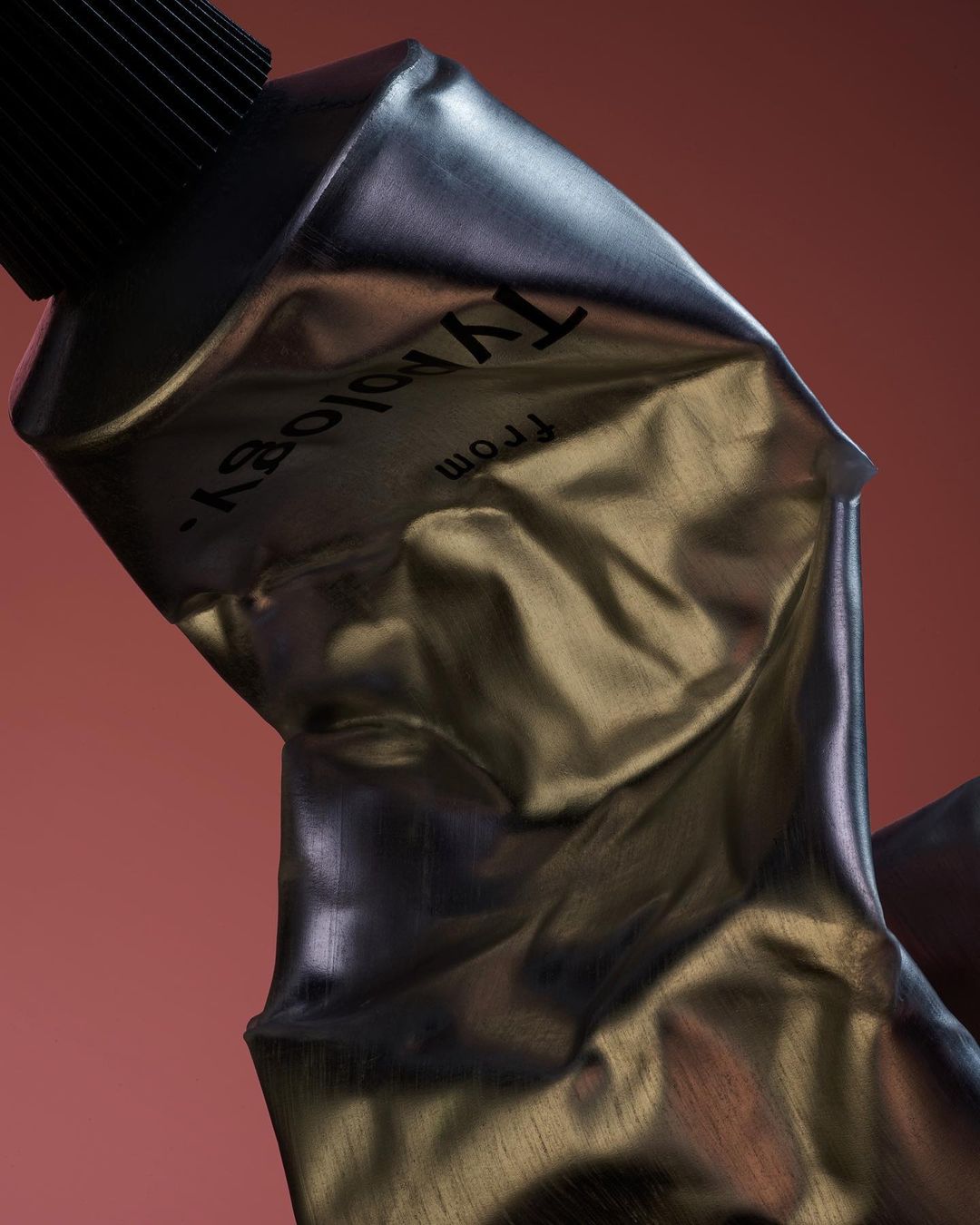 Silver metal tube against a terracotta backdrop. Texture is wrinkled, and the cap is black. The brand name "Typology" is printed.
