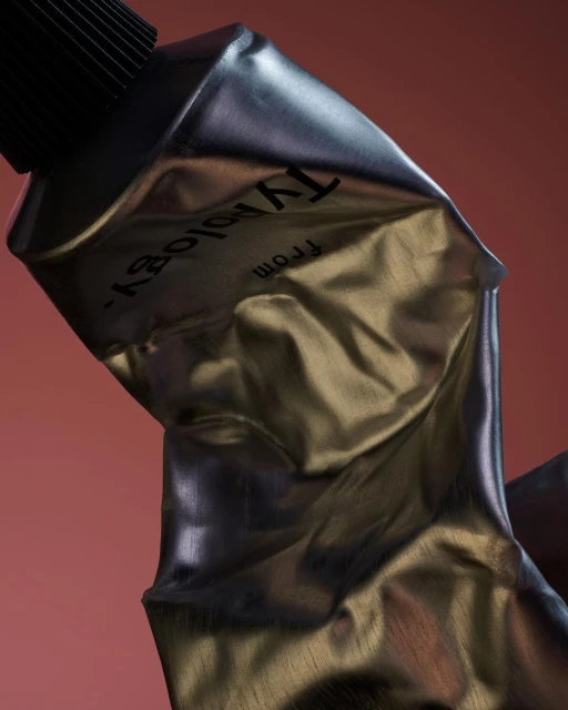 Silver metal tube against a terracotta backdrop. Texture is wrinkled, and the cap is black. The brand name "Typology" is printed.