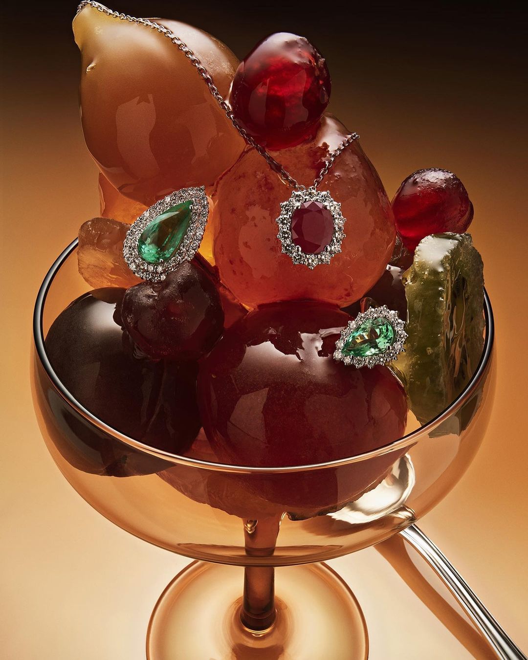 Jewelry displayed on fruit in a glass with a spoon, set against a warm gradient background, showcasing luxury and culinary art.