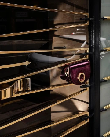 A close-up shot of a purple crossbody bag hanging on a gold metal display rack, creating an elegant and sophisticated fashion display.
