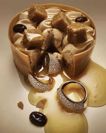 Diamond-paved gold jewelry rings and drop earrings displayed in a conceptual food setting with dessert ingredients and sauce.