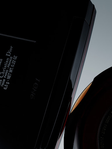 Close-up of black Christian Dior compact case with rounded makeup container, against a grey gradient background in a studio setting.