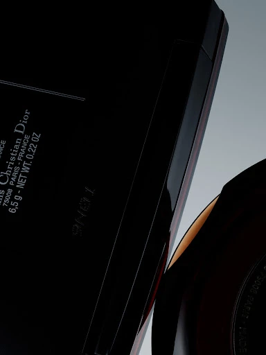 Close-up of black Christian Dior compact case with rounded makeup container, against a grey gradient background in a studio setting.
