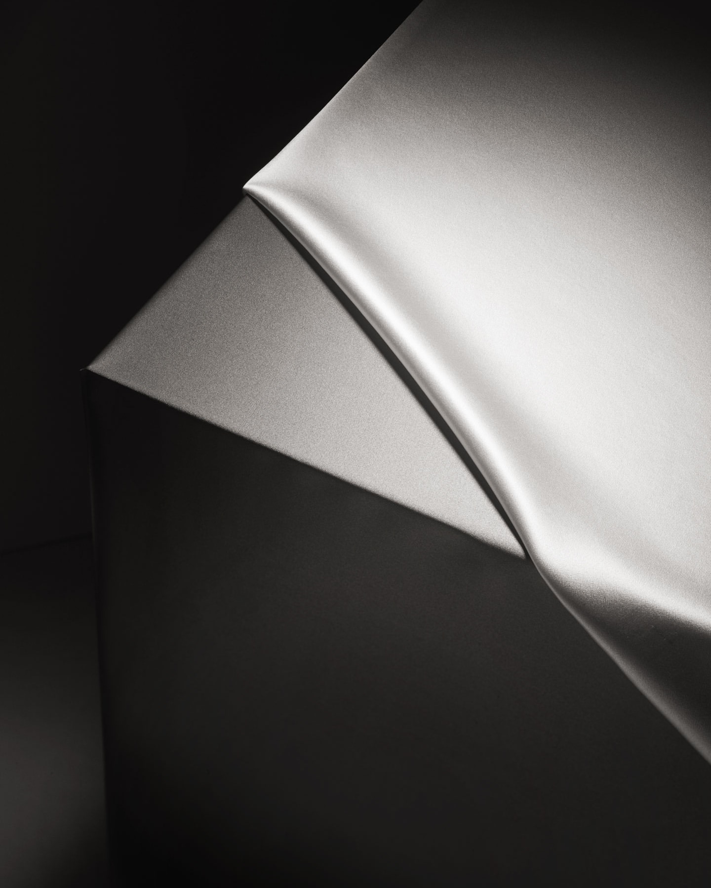 Elegant, draped gray silk fabric against a dark gray background in a minimalist studio setting, showcasing smooth textures and chiaroscuro lighting.