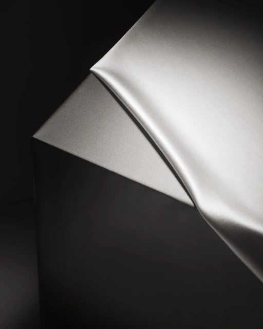 Elegant, draped gray silk fabric against a dark gray background in a minimalist studio setting, showcasing smooth textures and chiaroscuro lighting.