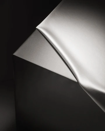 Elegant, draped gray silk fabric against a dark gray background in a minimalist studio setting, showcasing smooth textures and chiaroscuro lighting.