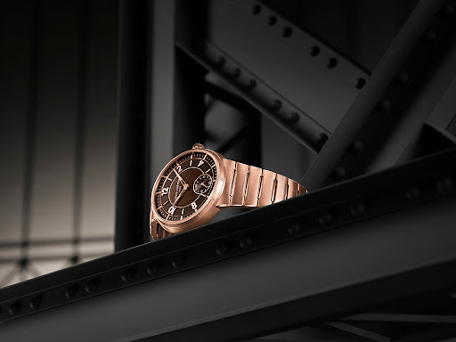 Elegant rose gold wristwatch with a brown dial on a black structural surface, highlighting watch design and craftsmanship.