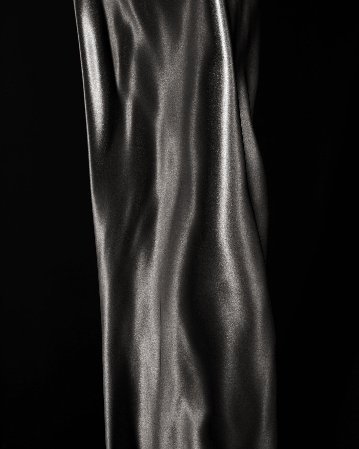 Elegant close-up of flowing, shiny grey fabric against a stark black background, highlighting texture and movement in a studio shot.