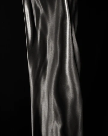 Elegant close-up of flowing, shiny grey fabric against a stark black background, highlighting texture and movement in a studio shot.