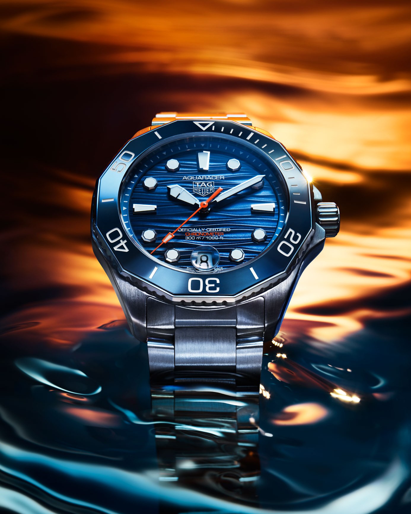 Elevated view of a TAG Heuer Aquaracer wristwatch featuring a blue dial, set against a dynamic background of reflective surfaces.