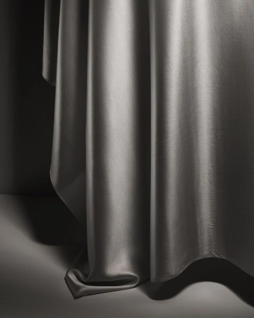 Abstract close-up of gray satin fabric draped on a gray surface, featuring soft lighting and shadows enhancing the material's sheen and texture.