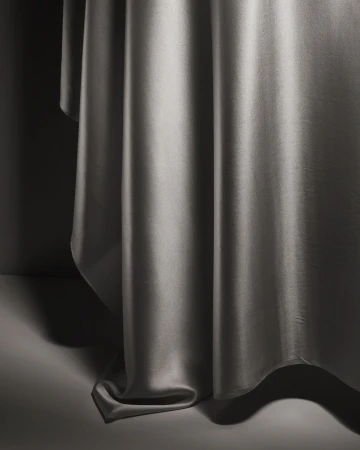 Abstract close-up of gray satin fabric draped on a gray surface, featuring soft lighting and shadows enhancing the material's sheen and texture.