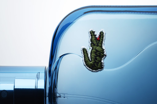 Close-up of a blue perfume bottle with a green crocodile emblem, presented against a soft white background, highlighting its elegant design.