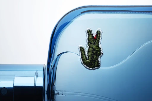 Close-up of a blue perfume bottle with a green crocodile emblem, presented against a soft white background, highlighting its elegant design.