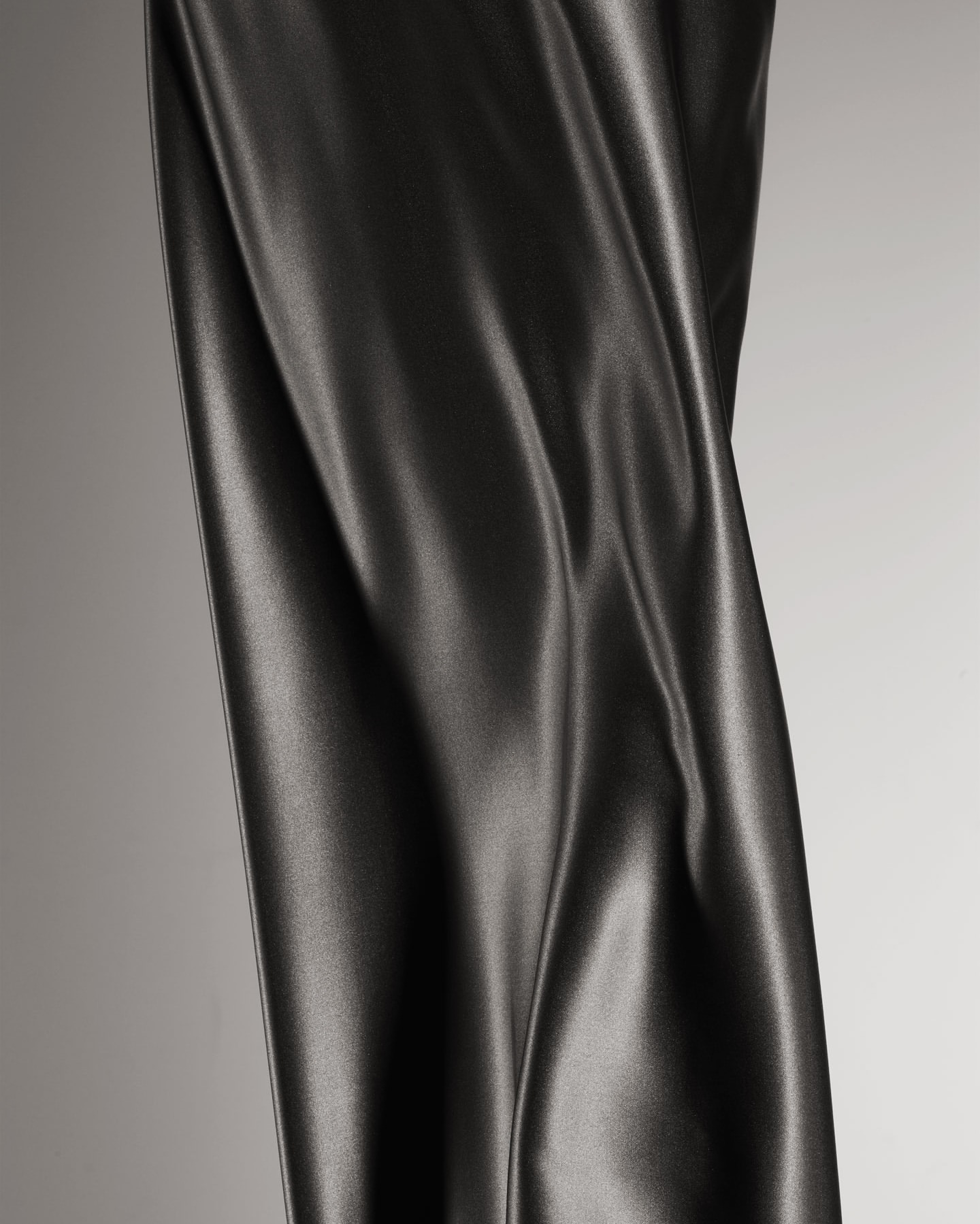Black leather textile swatch with draping folds and texture detail under studio lighting, neutral grey background, product shot, high detail.