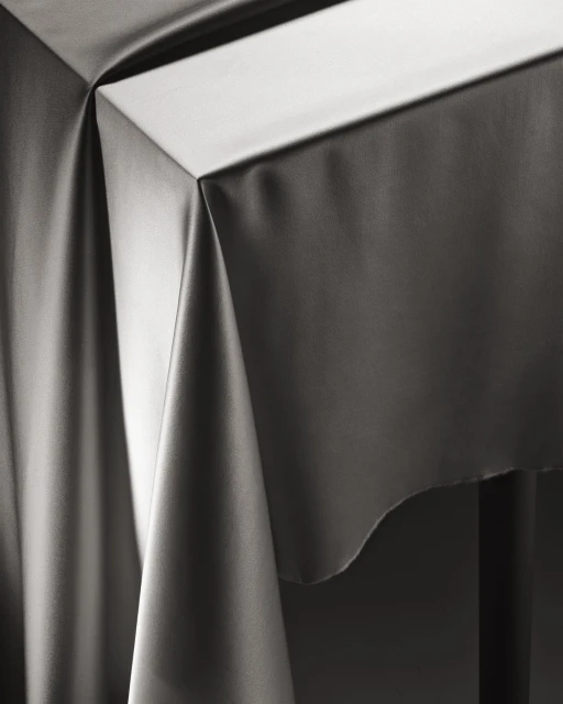 Elegant grey draped fabric over a table, creating soft folds and subtle lighting, ideal for background or design element.
