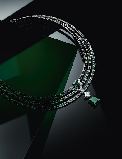 Elegant silver necklace with emerald and diamond gemstones against a dark backdrop with subtle green reflective accents.
