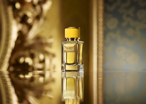 A rectangular glass perfume bottle with a yellow cap and gold plaque resting on a reflective surface