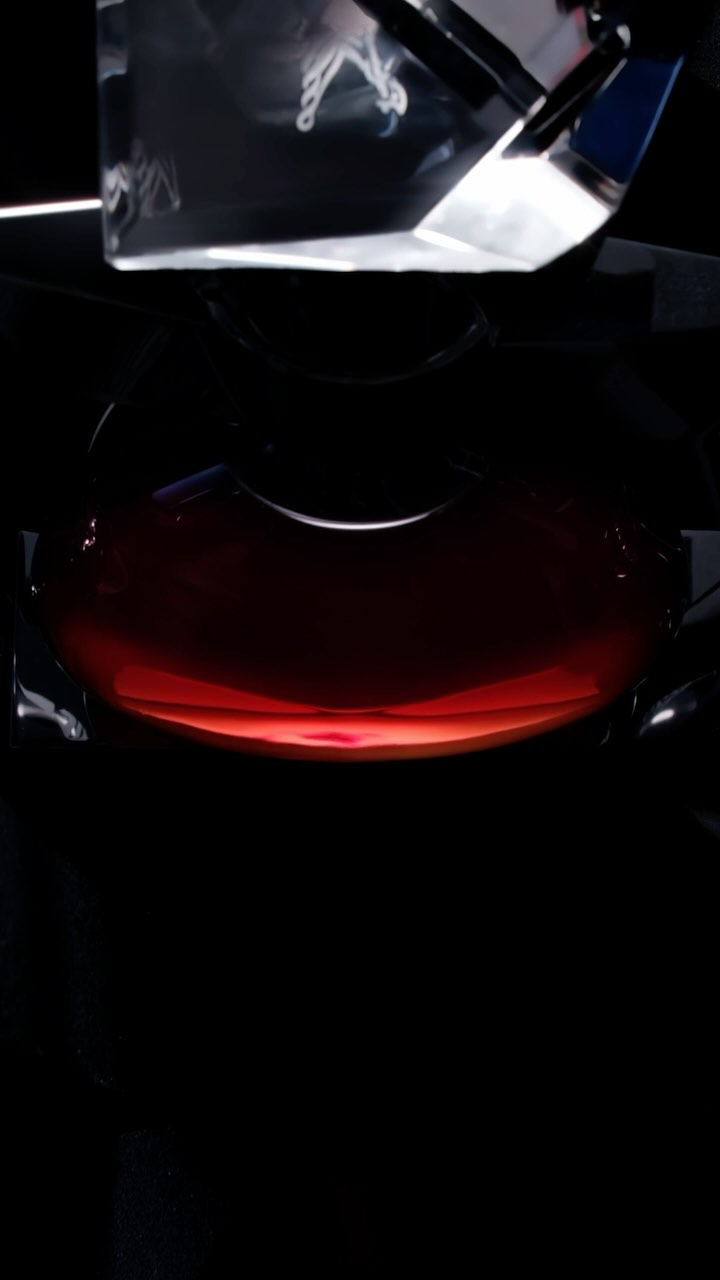 Low angle, close-up studio shot features a round, clear container filled with a dark red liquid with a clear rectangular object above it.