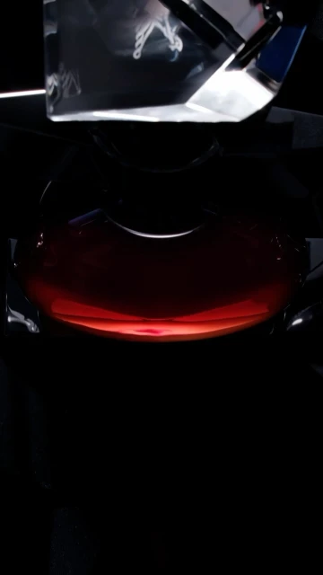 Low angle, close-up studio shot features a round, clear container filled with a dark red liquid with a clear rectangular object above it.