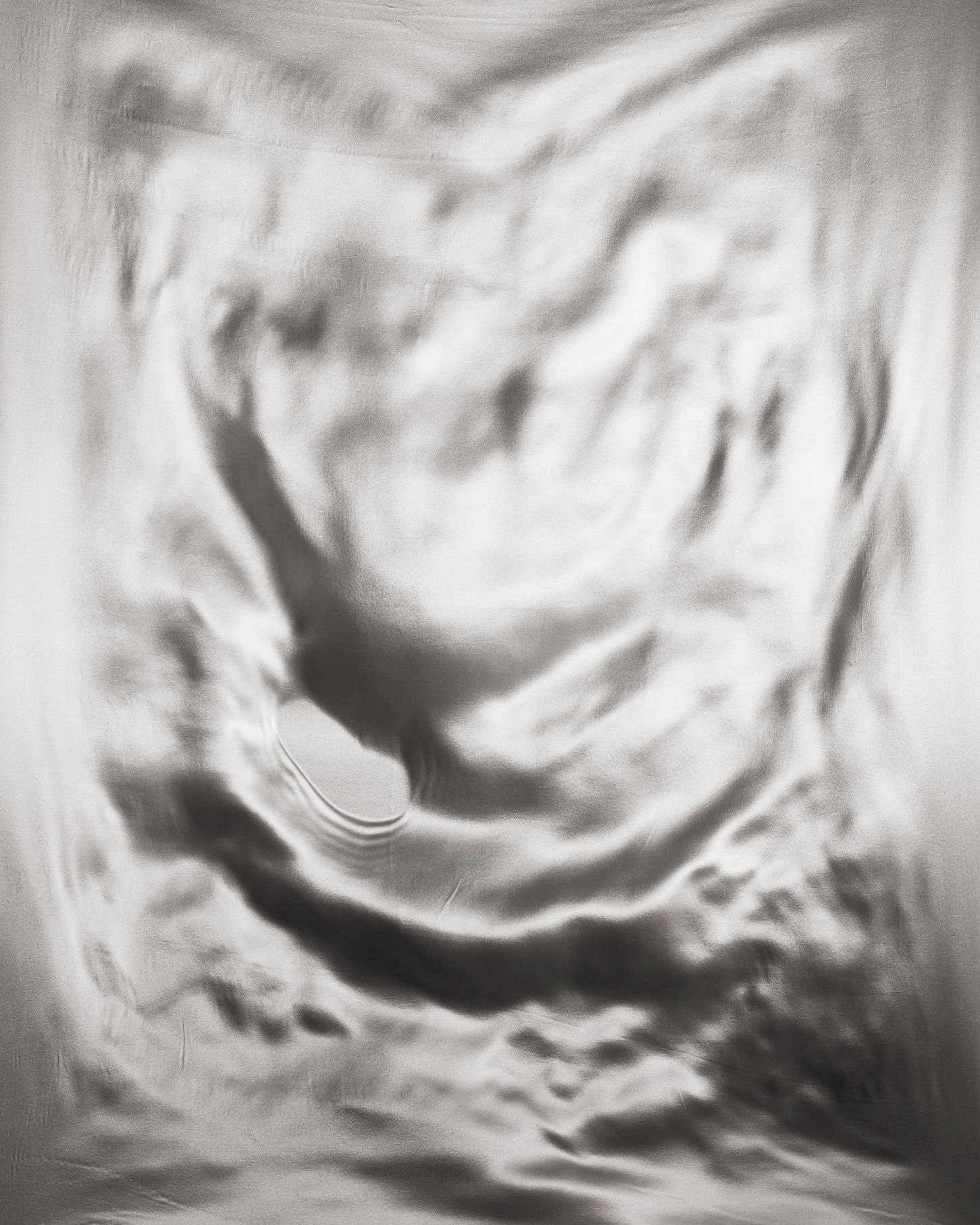Abstract silver fabric with rippled texture and a small hole, creating a soft, monochromatic, and visually interesting composition.