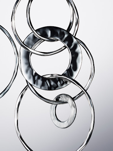 Abstract photo of interconnected silver metal rings on a light grey gradient background, creating a visually intriguing metallic sculpture.