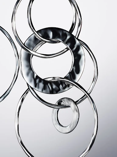 Abstract photo of interconnected silver metal rings on a light grey gradient background, creating a visually intriguing metallic sculpture.