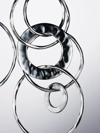 Abstract photo of interconnected silver metal rings on a light grey gradient background, creating a visually intriguing metallic sculpture.