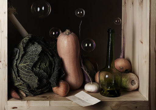 Still life photography of various vegetables including cabbage, squash, carrots, and turnips with a vintage bottle and floating bubbles.