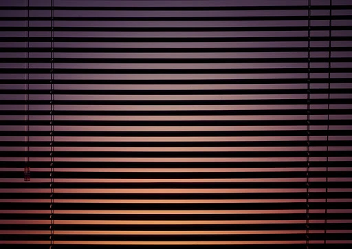 Closed window blinds filtering light into a room, creating horizontal lines and warm hues. Interior view during evening.