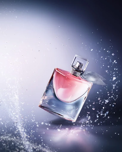 Elegant perfume bottle with square glass design, pink liquid, silver ribbon, and dynamic water droplets against a blue background.