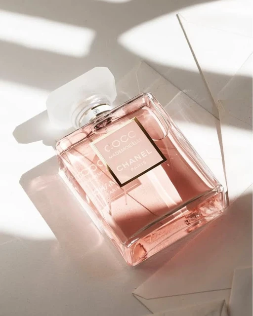 Elegant rectangular glass bottle of Coco Mademoiselle Chanel Paris perfume with translucent cap on a white surface with shadow.