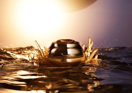La Mer cream jar on water with crystal accents, illuminated by soft golden light, showcasing luxury beauty product in a serene setting.