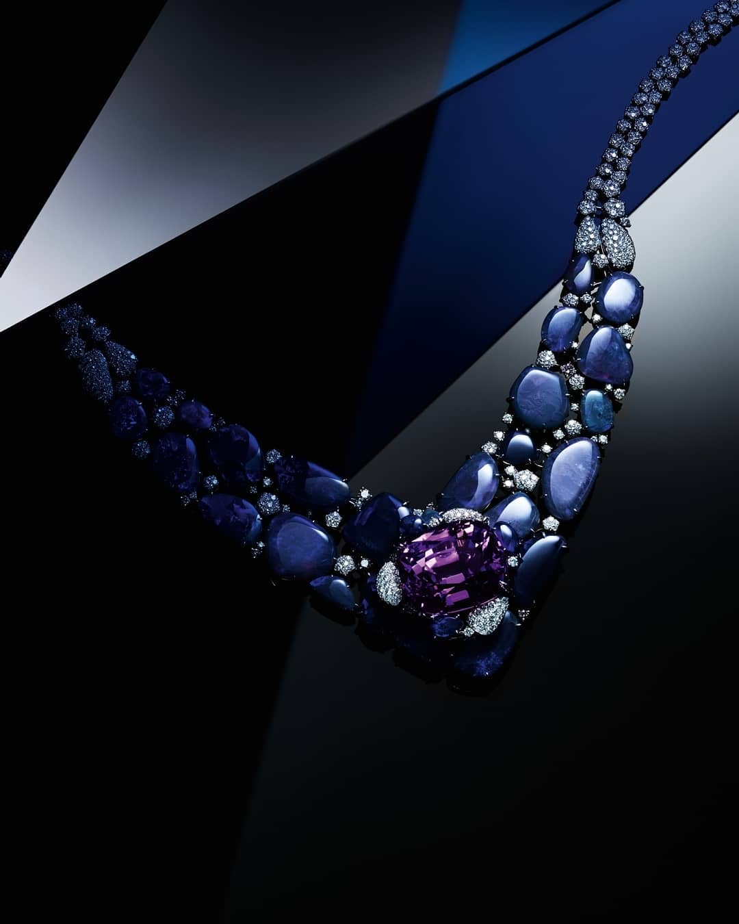 Elegant sapphire and diamond necklace on a glossy black surface, enhanced by geometric light patterns, luxurious jewellery advertisement.