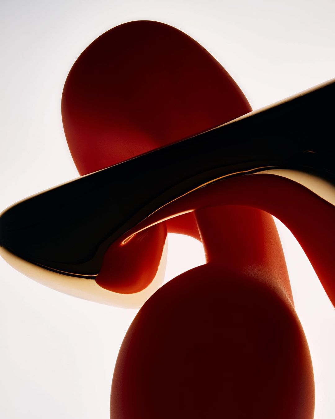Abstract sculpture with red curved forms and a glossy black bar in a brightly lit studio setting, highlighting its modern design.