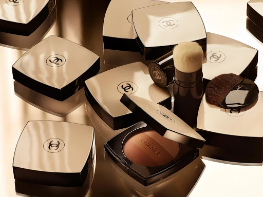 Several Chanel compacts and brushes in a golden-toned, high-key product shot for beauty and cosmetic advertising, showcasing luxury branding.