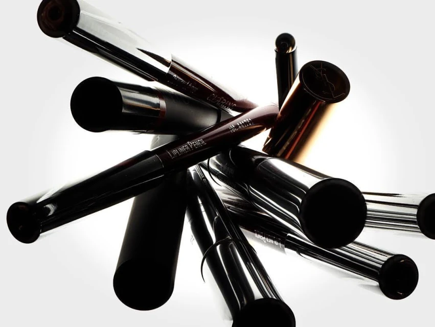 Arrangement of lip liner pencils in black, silver, and gold colors against a bright white background, beauty and cosmetic product.